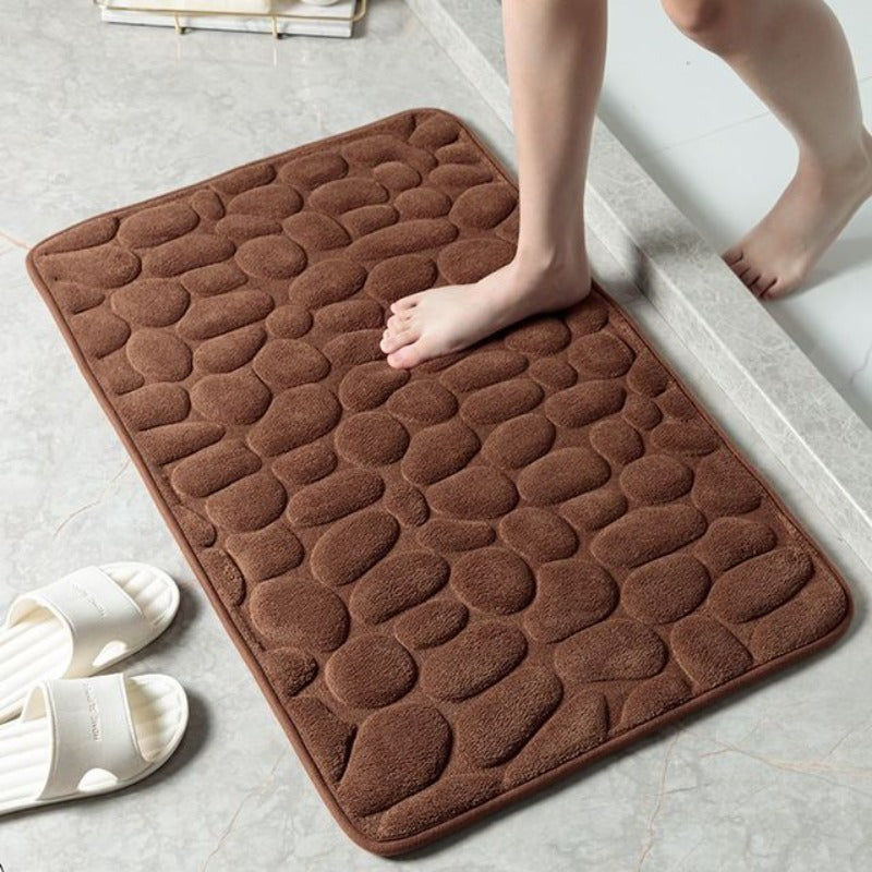 Badematte im Kieselstein-Design neben Badewanne auf Badezimmerboden